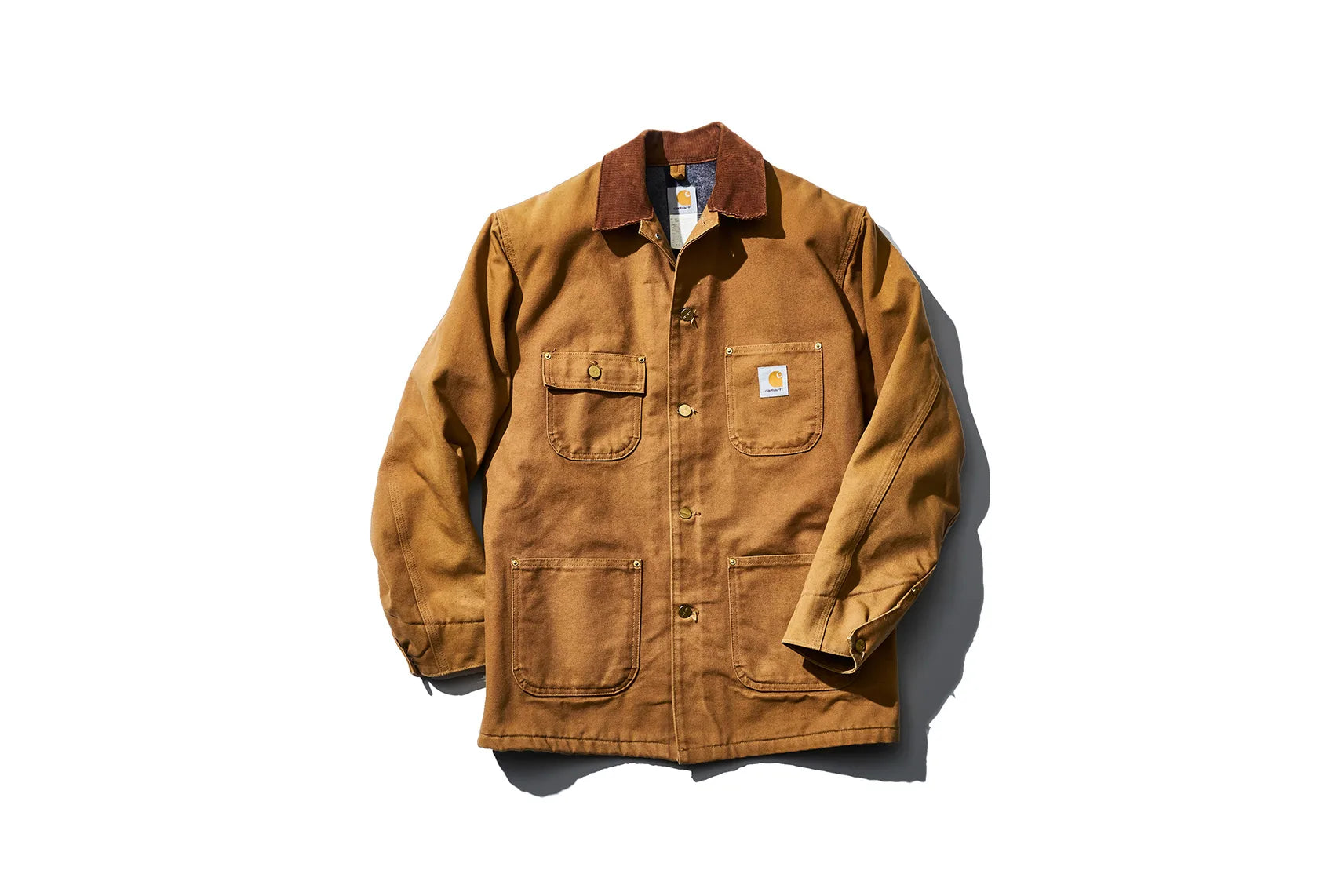 Carhartt brown duck canvas chore coat with brown corduroy collar, button front, four front utility pockets, and Carhartt logo patch on the left chest pocket.