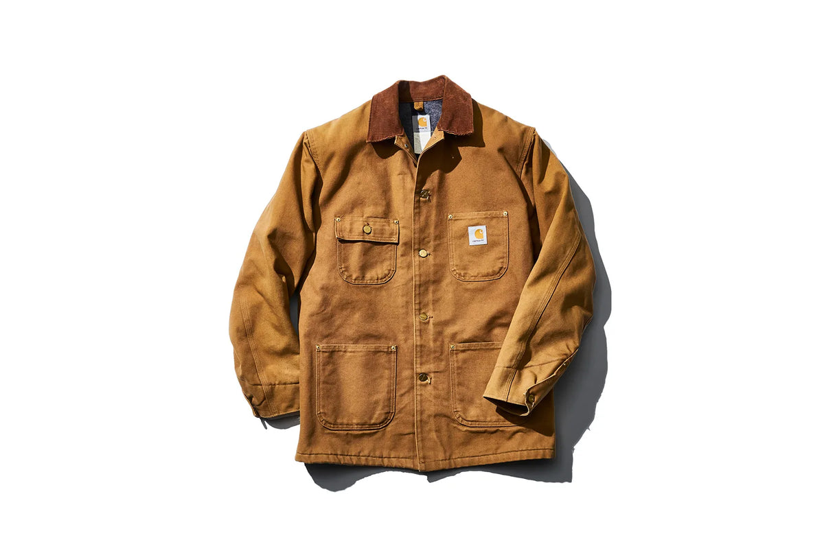 Carhartt brown duck canvas chore coat with brown corduroy collar, button front, four front utility pockets, and Carhartt logo patch on the left chest pocket.