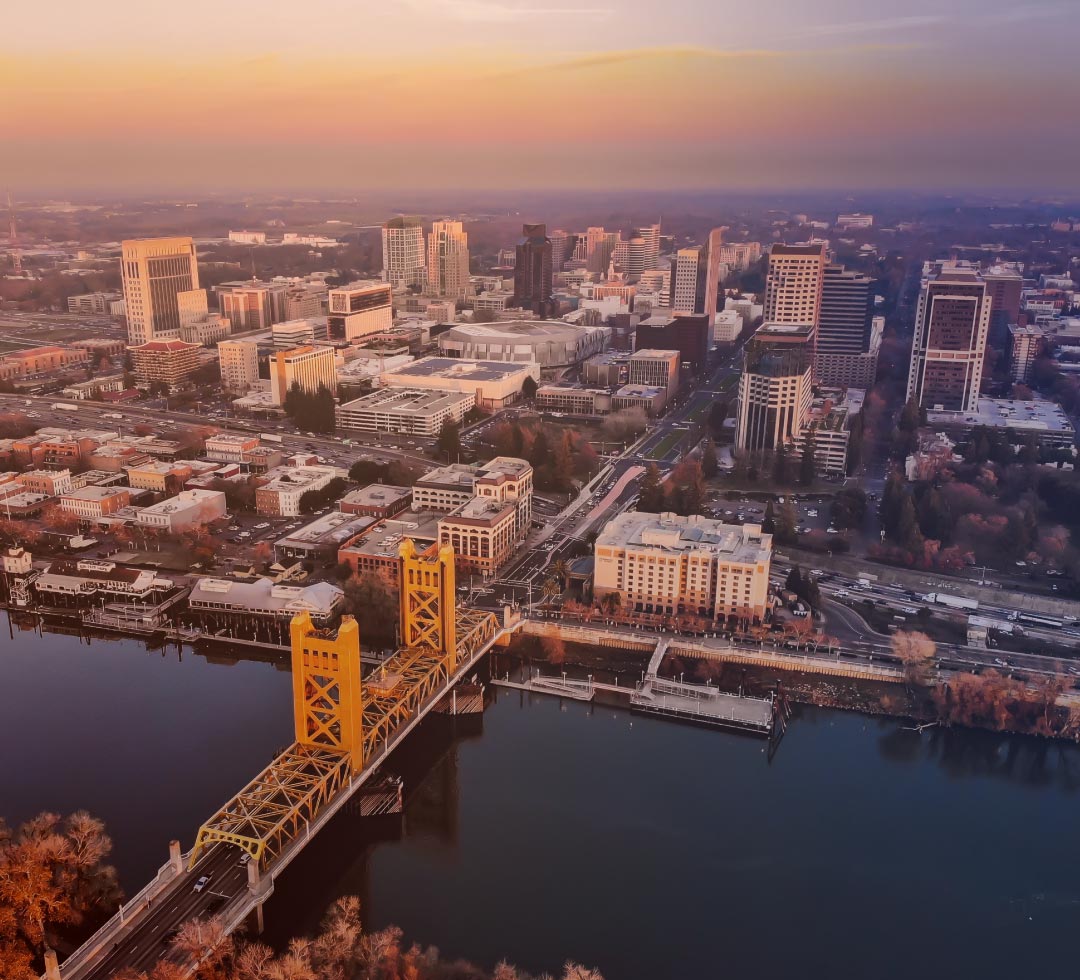 Cityscape with a prominent yellow bridge over a river at sunset.