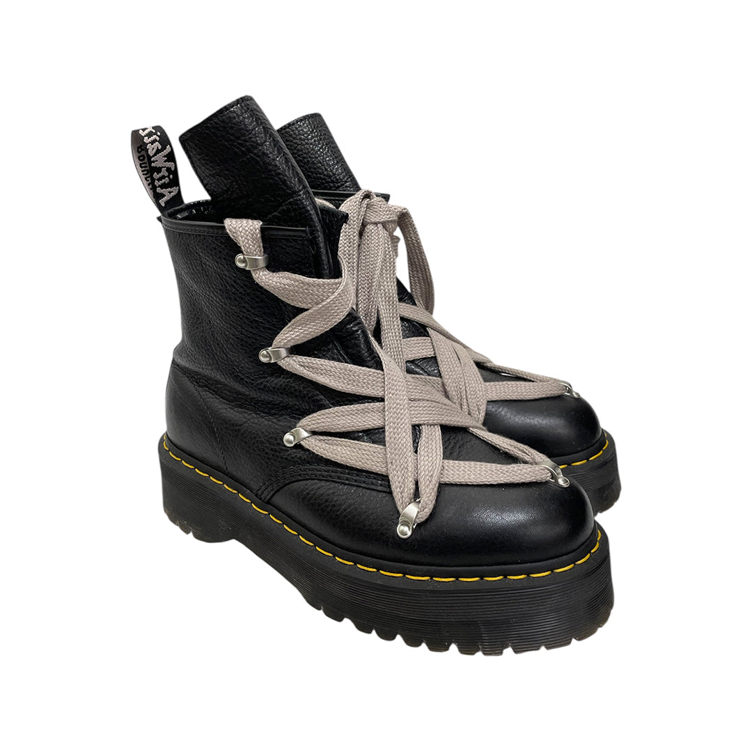 A pair of black leather Dr. Martens x Rick Owens lace-up ankle boots with wide, crisscrossed light gray laces and a yellow welt stitch on a white background.