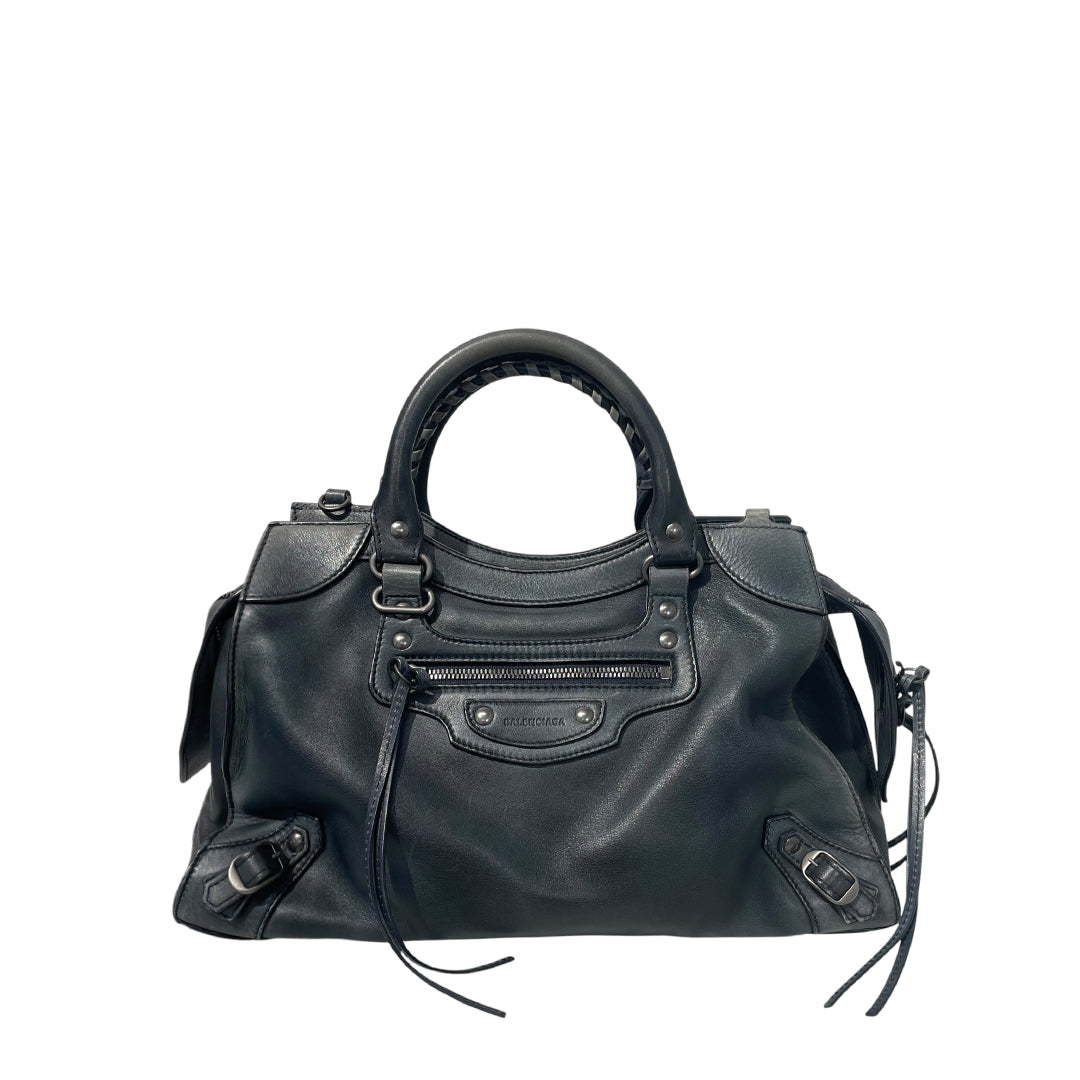 A black leather Balenciaga handbag with dual top handles, a front zip pocket, and silver-tone hardware, photographed against a plain white background.