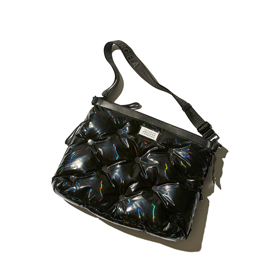 A black puffer-style shoulder bag with a glossy, quilted bubble texture and holographic rainbow accents, featuring a black shoulder strap with white lettering, set against a plain white background.