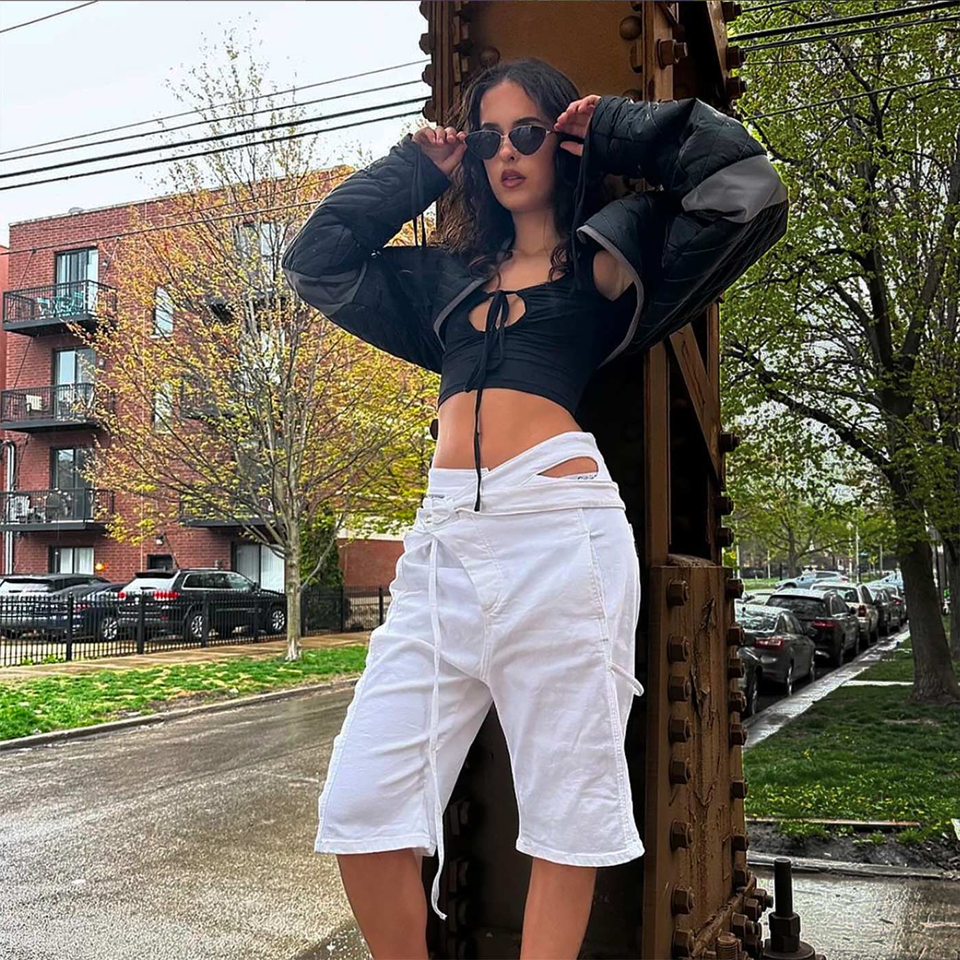 Woman in black crop top and white shorts posing on a large metal object with urban background
