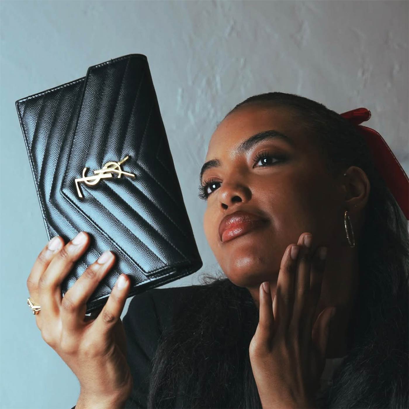 Woman holding a black YSL wallet against a neutral background